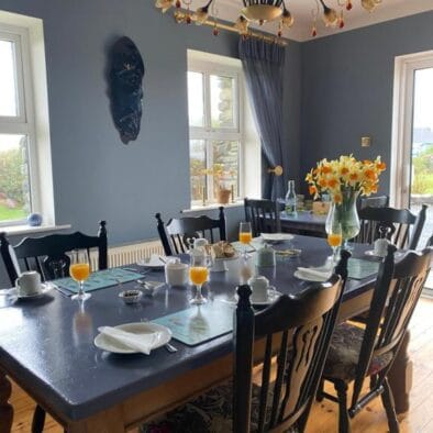 Breakfast table at An Riasc B&B with orange juice and daffodils in a bright blue room