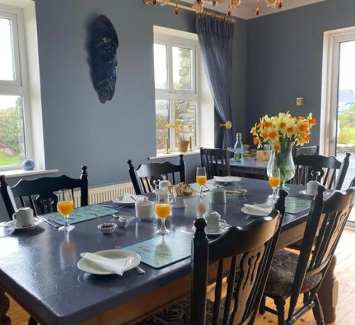 Breakfast table at An Riasc B&B with orange juice and daffodils in a bright blue room